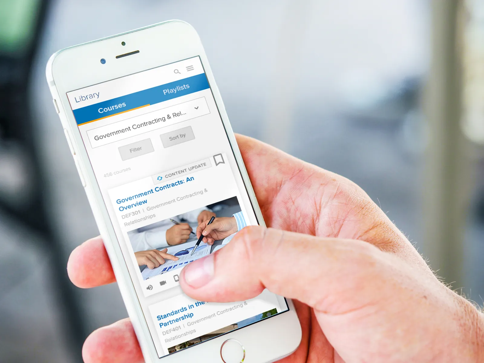 A hand holding a phone showing the training app's library and playlists.