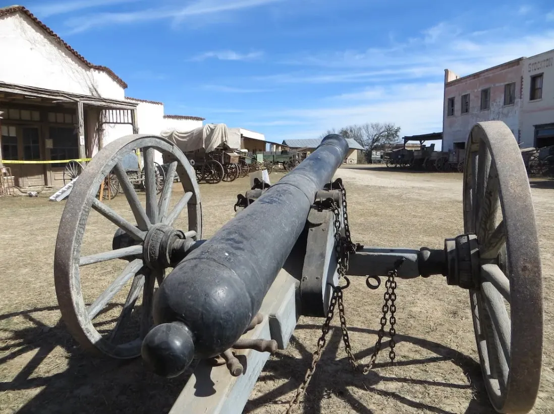 A cannon on a wooden carriage in the yard of a frontier-era historic site.
