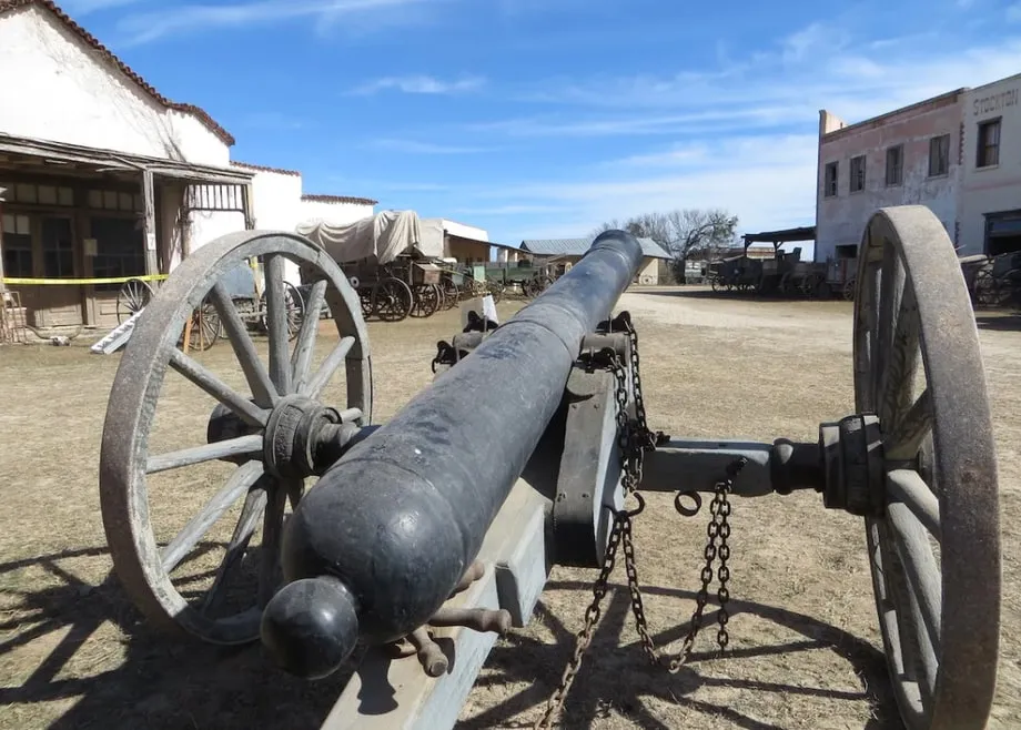 A cannon on a wooden carriage in the yard of a frontier-era historic site.